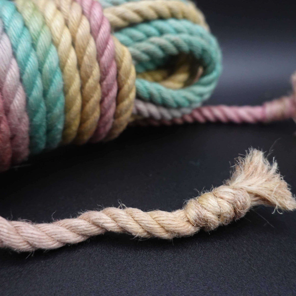 Close-up of colorful jute shibari rope displayed on a dark background, emphasizing its natural dyes and texture.